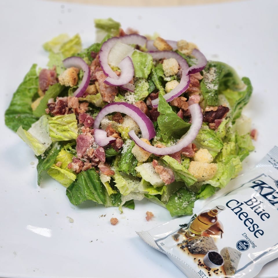 Caesar salad with red onions, bacon bits, croutons, and a packet of blue cheese dressing.