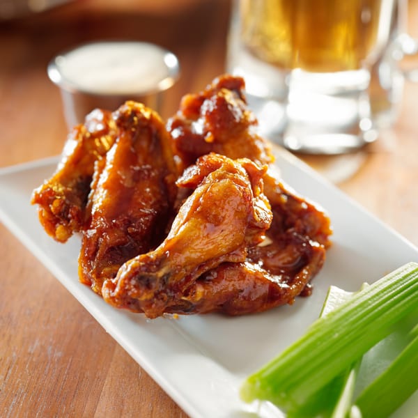 Slices New York's glazed chicken wings with celery sticks and dipping sauce on a white plate.
