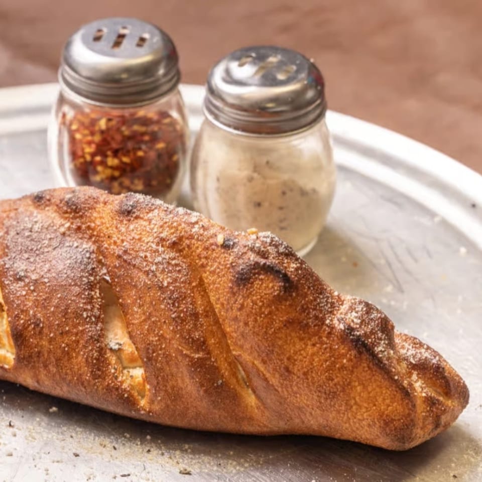 A golden-brown calzone dusted with parmesan cheese, with shakers of red pepper flakes and garlic powder.