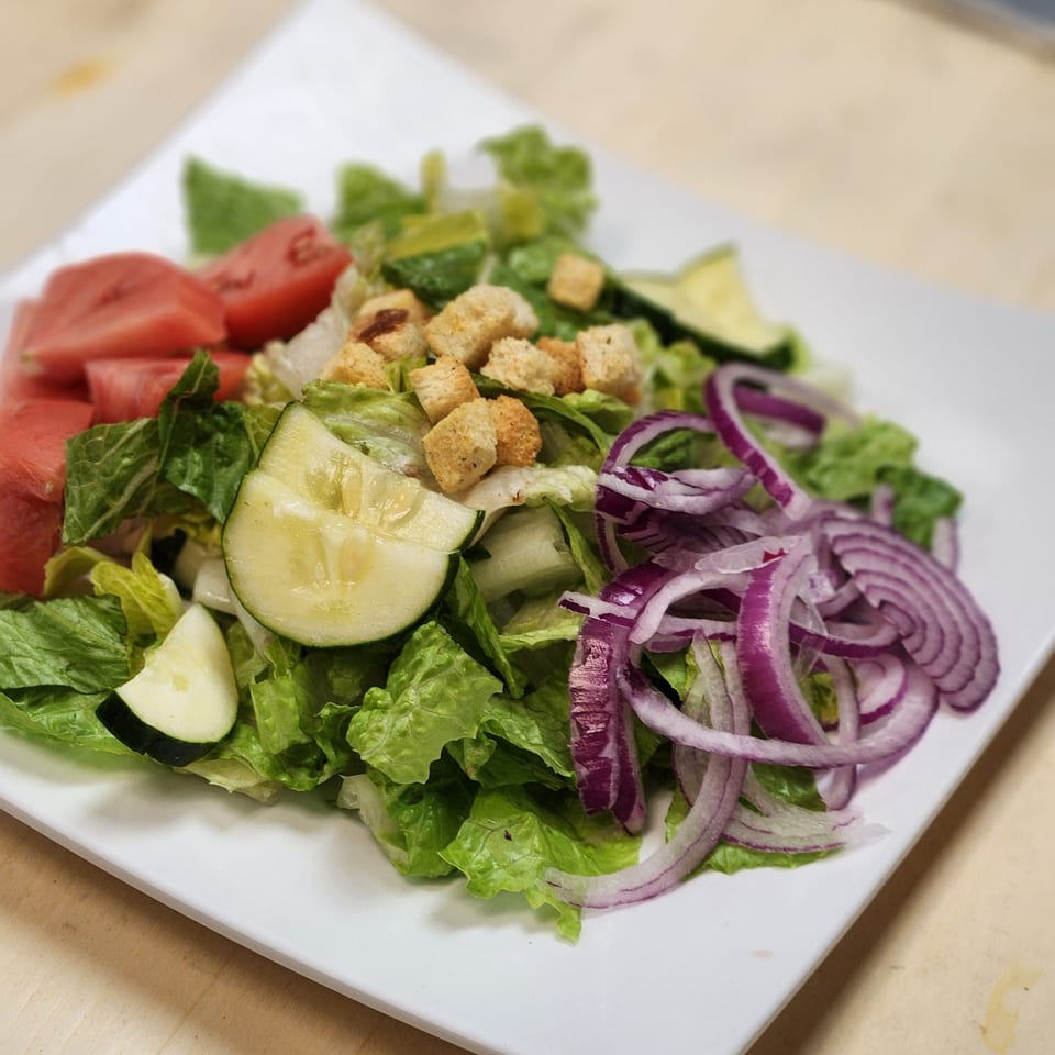 Fresh garden salad with lettuce, tomatoes, cucumbers, red onions, and croutons on a white plate.