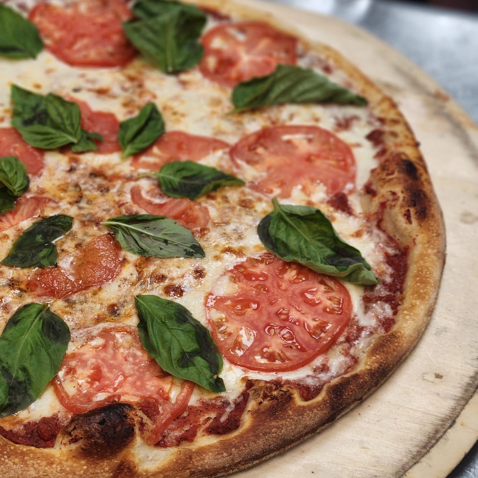 Close-up of a Slices New York pizza with fresh tomatoes, mozzarella, and basil on a wooden peel.