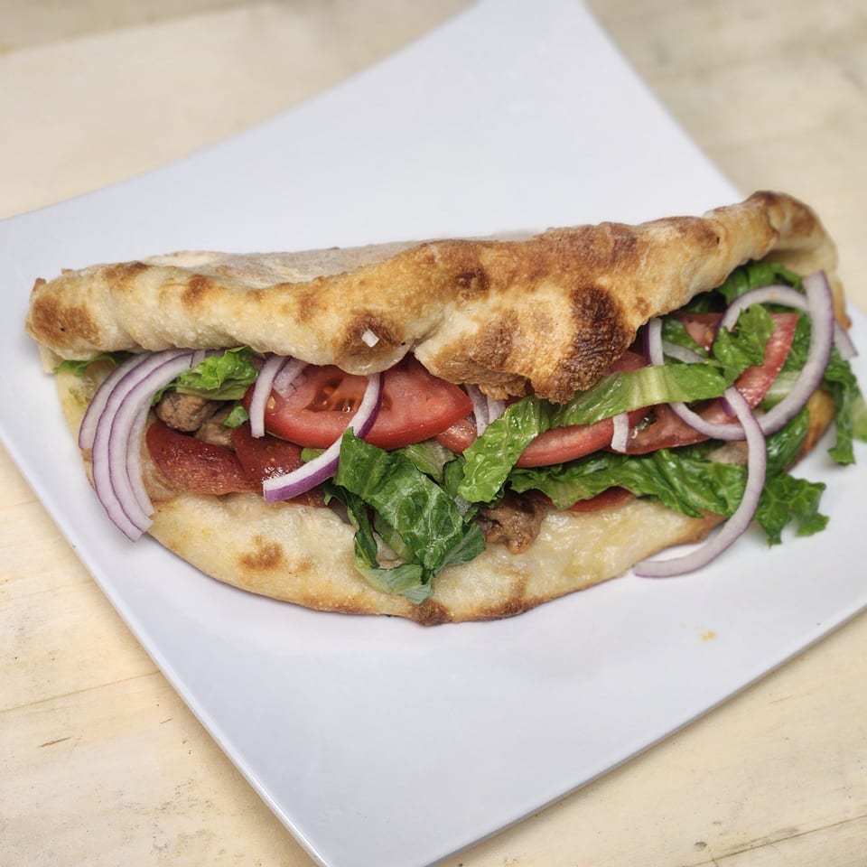 A Slices New York calzone filled with meat, lettuce, tomatoes, and red onions on a white plate.